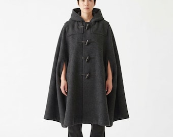 May include: A dark charcoal grey wool-blend hooded cape featuring a front closure with four black toggle buttons and loops. The garment has an A-line silhouette with arm slits on the sides, providing a structured yet flowing drape over the shoulders.
