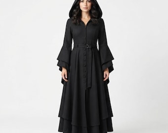 May include: A floor-length black coat featuring a pointed hood, long flared sleeves with tiered layers, and a front button closure. The garment includes a matching fabric belt with a buckle at the waist, creating a structured silhouette.