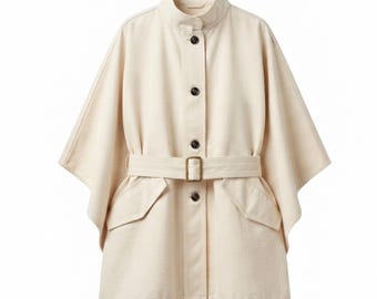 May include: A cream-coloured cape jacket featuring a stand-up collar, a front button placket with dark brown buttons, and a matching fabric belt with a rectangular buckle. The garment includes two front flap pockets and wide, open-style sleeves.