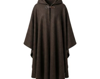 May include: A dark brown hooded cloak featuring a textured fabric finish. The garment includes a front closure consisting of a brown leather strap and a metallic buckle, providing a secure fastening at the neckline while maintaining a draped silhouette.