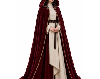 May include: A floor-length, deep burgundy velvet cloak featuring a hood, gold-toned trim, and a decorative metal clasp at the neck. Underneath, a long-sleeved, light beige tunic is cinched at the waist with a dark brown leather belt.