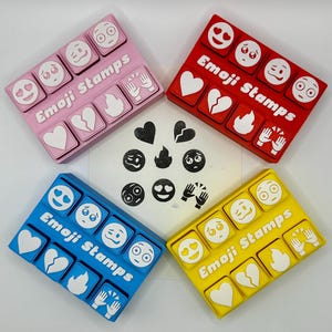 May include: Four sets of emoji stamps in pink, red, blue, and yellow. Each set has a different colour base and features various emoji designs, including hearts, flames, and faces. The text "Emoji Stamps" is printed on each set.
