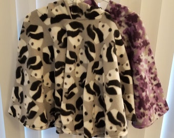 May include: Two fleece hooded ponchos, one with a black and white abstract pattern and the other with a purple and white floral pattern.
