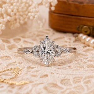 May include: A silver-toned ring featuring a large marquise-cut center stone flanked by three smaller marquise-cut stones on each side. The band is thin and metallic, showcasing a clear, faceted design that reflects light across its surface.