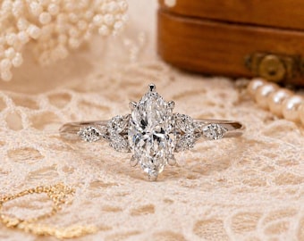 Può includere: Un anello color argento con una grande pietra centrale taglio marquise affiancata da tre pietre più piccole taglio marquise su ciascun lato. La fascia è sottile e metallica, con un design chiaro e sfaccettato che riflette la luce.