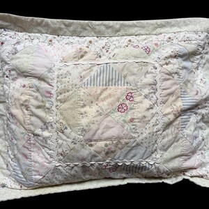 Peut inclure: Un oreiller rectangulaire avec un motif patchwork. L'oreiller présente divers motifs floraux et rayés dans des couleurs pastel douces, notamment du rose, crème et bleu clair. Les bords sont ornés d'une dentelle festonnée, créant une esthétique vintage.