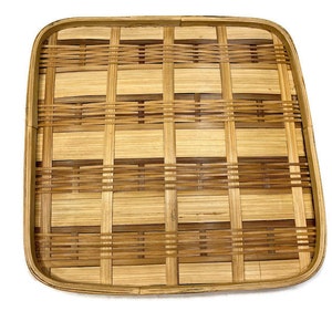 May include: A square, woven bamboo tray with a natural brown color. The tray has a grid pattern and is made of thin strips of bamboo.