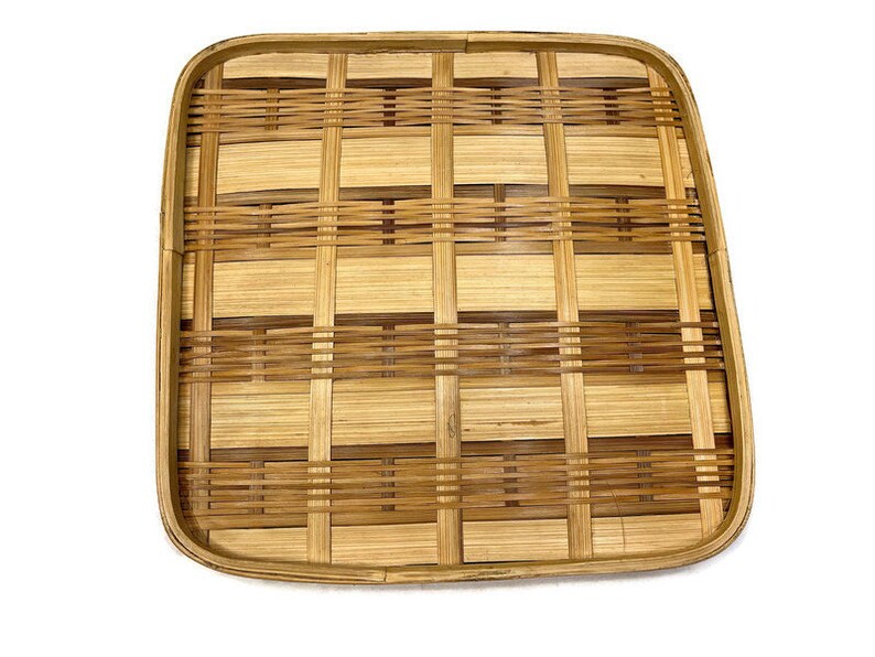 May include: A square, woven bamboo tray with a natural brown color. The tray has a grid pattern and is made of thin strips of bamboo.