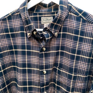 Puede incluir: Una camisa de manga larga a cuadros azules y beige con el texto "L.L.Bean" en la parte delantera.