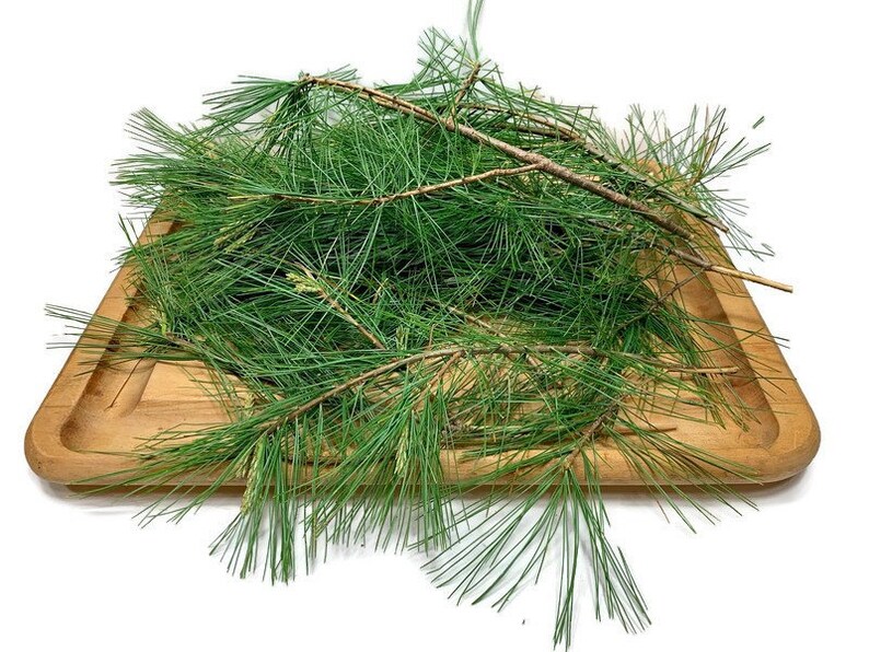 May include: A pile of fresh green pine needles on a wooden tray. The needles are long and thin, and they are arranged in a random pattern. The tray is made of light brown wood and has a smooth surface.