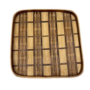 May include: A square woven bamboo tray with a natural brown and light brown color scheme. The tray has a woven pattern with a grid design.