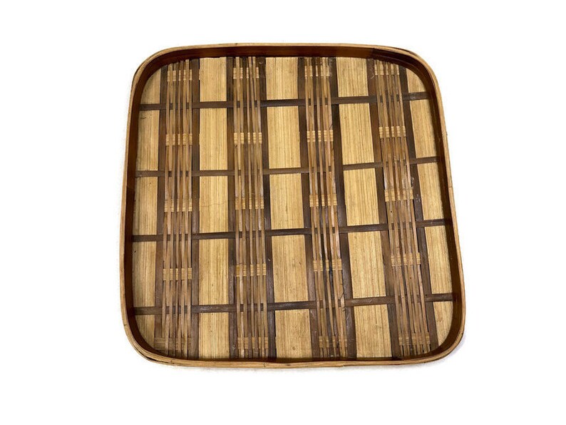 May include: A square woven bamboo tray with a natural brown and light brown color scheme. The tray has a woven pattern with a grid design.