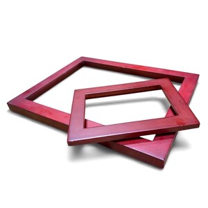May include: Two rectangular picture frames with a smooth, dark reddish-brown finish. The frames are positioned at an angle, with the smaller frame resting partially on top of the larger frame, both featuring flat, wide borders and clean edges.