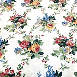 Puede incluir: Tela blanca con un estampado floral. El diseño presenta racimos de rosas rojas, amarillas y azules con hojas verdes y pequeñas bayas rojas. Las flores están dispuestas sobre un fondo blanco.