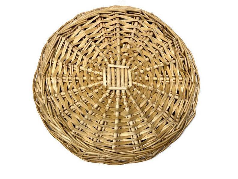 May include: A round, woven wicker basket with a natural brown color. The basket is made of tightly woven strips of wicker, creating a smooth, even surface.