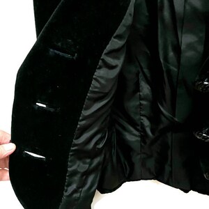 May include: A black velvet jacket with a button closure and decorative black buttons. The jacket is lined with a black fabric.