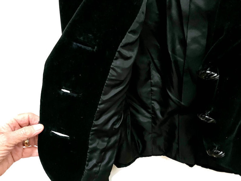 May include: A black velvet jacket with a button closure and decorative black buttons. The jacket is lined with a black fabric.