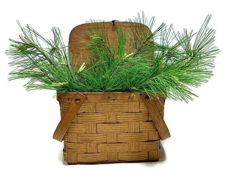 May include: A brown wicker picnic basket with a hinged lid and two handles. The basket is filled with green pine branches.