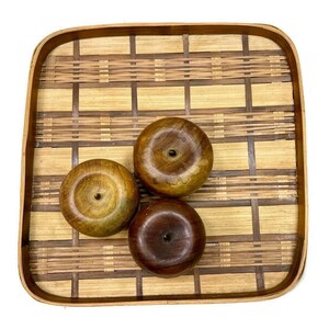 May include: Three wooden bowls with a natural wood finish are arranged on a woven bamboo tray. The tray has a light brown color and a square shape.