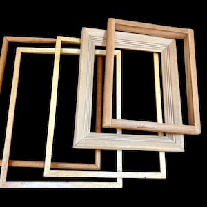 May include: A collection of five wooden picture frames in various shades of light brown and beige, arranged against a black background. The frames are rectangular, with visible wood grain and varying levels of detail.