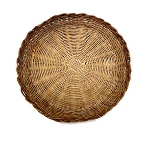 May include: A round woven wicker basket with a natural brown color. The basket has a circular shape and is made of tightly woven strands of wicker.