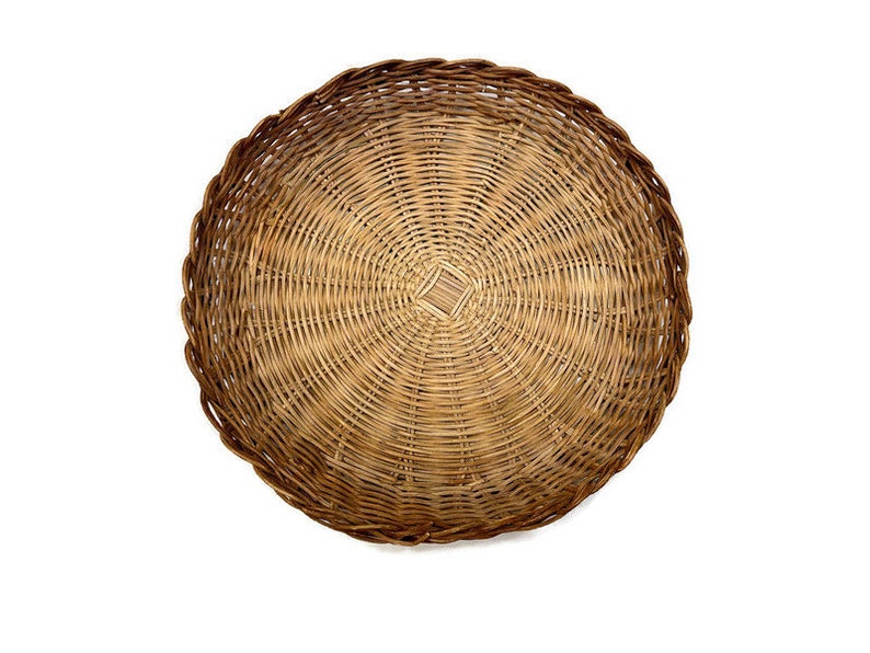May include: A round woven wicker basket with a natural brown color. The basket has a circular shape and is made of tightly woven strands of wicker.