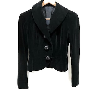 May include: A black velvet blazer with a wide collar and three buttons. The blazer has a fitted silhouette and a cropped length.