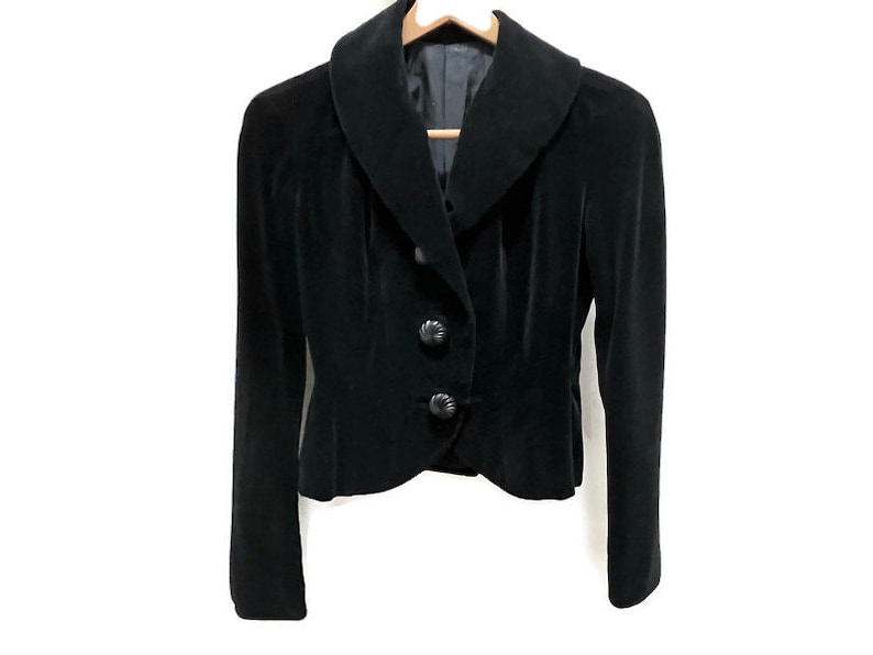 May include: A black velvet blazer with a wide collar and three buttons. The blazer has a fitted silhouette and a cropped length.