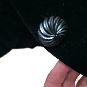 May include: A black velvet jacket with a large, black, swirl-shaped button.