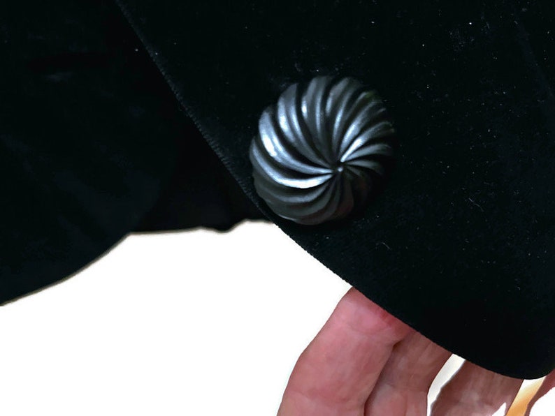 May include: A black velvet jacket with a large, black, swirl-shaped button.