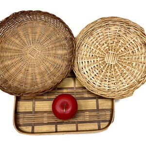 May include: Three round woven wicker baskets with a natural brown color. The baskets are arranged on a rectangular woven bamboo tray with a brown and natural color pattern. A red apple is sitting on the tray.