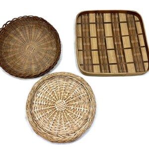 May include: Three woven baskets, two round and one square. The round baskets are made of natural brown wicker, while the square basket is made of a darker brown woven material with a geometric pattern.