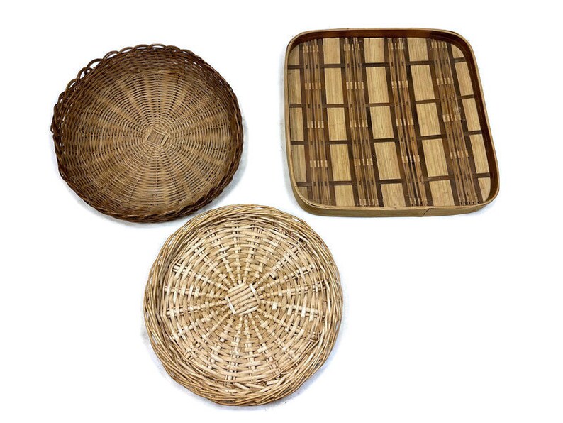 May include: Three woven baskets, two round and one square. The round baskets are made of natural brown wicker, while the square basket is made of a darker brown woven material with a geometric pattern.
