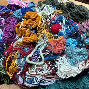 Könnte beinhalten: Ein großer Haufen bunter Garne in verschiedenen Texturen und Farbtönen, darunter Rosa, Lila, Blau, Grün, Orange und Rot. Das Garn scheint eine Mischung aus verschiedenen Arten wie Wolle und Baumwolle zu sein, geeignet für Strick- oder Häkelprojekte.