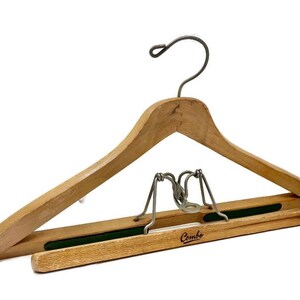 May include: A wooden clothes hanger with a metal hook and a hinged bar for pants. The hanger has a natural wood finish and a green felt strip on the bar. The word "Combo" is printed on the bar.