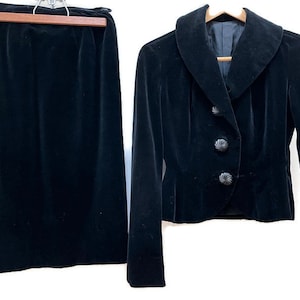May include: A black velvet skirt and jacket set. The jacket has a large collar and a button closure. The skirt is a simple A-line style.