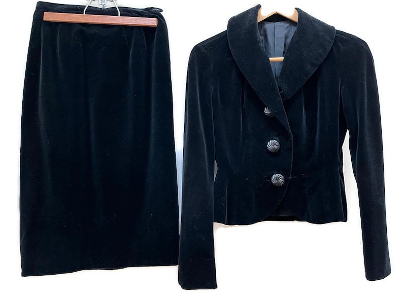 May include: A black velvet skirt and jacket set. The jacket has a large collar and a button closure. The skirt is a simple A-line style.