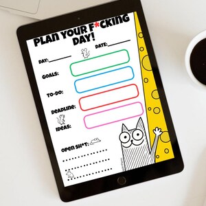 May include: A black tablet displaying a daily planner with the text "PLAN YOUR F*CKING DAY!". The planner includes sections for day, goals, to-do, deadline, and ideas, with a cartoon cat illustration. A cup of coffee is visible.