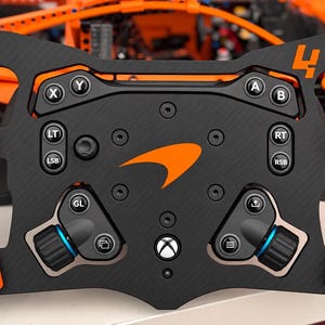 Könnte beinhalten: Ein schwarz-oranges Rennlenkrad mit dem McLaren-Logo in der Mitte, der Zahl 4 in der oberen rechten Ecke und standardmäßigen Xbox-Tastenbelegungen, einschließlich X, Y, A, B, LT, RT, LSB, RSB und einer zentralen Xbox-Logo-Taste.