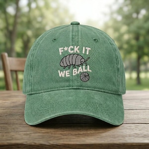 May include: Green baseball cap with the text "F*CK IT WE BALL" and an illustration of a pill bug and a basketball. The cap is made of a soft, worn material and has a curved brim.