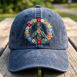May include: A dark blue denim baseball cap featuring an embroidered peace sign composed of colorful flowers and green leaves. The floral design includes red, yellow, pink, orange, and white blossoms arranged in a circular pattern on the front panel.