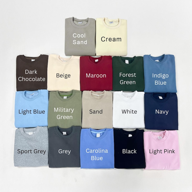 May include: A collection of seventeen crewneck sweatshirts arranged in a grid, featuring various solid colors labeled as Cool Sand, Cream, Dark Chocolate, Beige, Maroon, Forest Green, Indigo Blue, Light Blue, Military Green, Sand, White, Navy, Sport Grey, Grey, Carolina Blue, Black, and Light Pink.