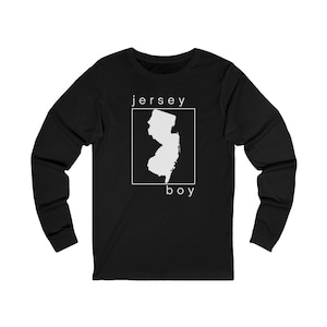 Peut inclure: T-shirt noir à manches longues avec le texte "jersey boy" et un contour blanc de l'État du New Jersey. Le contour de l'État est à l'intérieur d'un carré blanc. Le t-shirt est en matière douce et confortable.