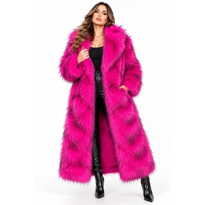May include: A long, vibrant hot pink faux fur coat featuring a thick, plush collar and lapels. The coat has a shaggy texture with subtle black-tipped fibres throughout, extending to the mid-calf, worn over a black top and black leather trousers.