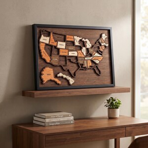 May include: A framed wooden wall art piece featuring a multi-layered map of the United States. The map displays individual states in varying shades of natural wood, including light, medium, and dark brown tones, set against a dark wood background.