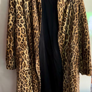 Pode incluir: Um casaco comprido com estampa de leopardo e forro interior preto. O casaco está pendurado em um cabide rosa. A estampa de leopardo apresenta manchas marrons e pretas em um fundo bege. O casaco está aberto, revelando o forro preto.