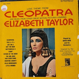 May include: A vintage vinyl record album cover for "Cleopatra" featuring Elizabeth Taylor. The album is yellow with red text, listing songs and other films. The cover art includes a portrait of Elizabeth Taylor in character.