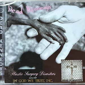 May include: CD case for the Dead Kennedys album "Plastic Surgery Disasters and the 12" EP". The cover art features a black and white image of two hands, one holding the other. The album title and band name are in pink and white text.