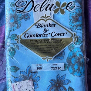 K&ouml;nnte beinhalten: Hellblaue Deluxe Decke und Bettdeckenbezug mit blau-braunem Blumenmuster. Die Verpackung tr&auml;gt die Aufschrift "Blanket & Comforter Cover". Die Ma&szlig;e sind 183 x 229 cm.