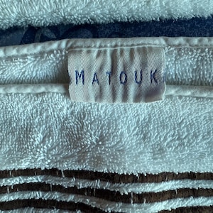 May include: Close-up of white terry cloth towels with the brand name "MATOUK" visible on a label. The towels have brown stripes and a soft, textured appearance, suggesting a focus on comfort and quality.